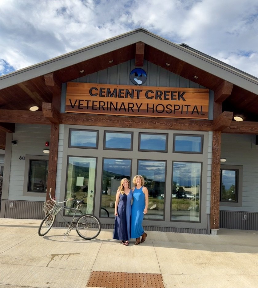Dr. Kara Erickson and Shawna Castillo standing together outside the entrance of Cement Creek Veterinary Hospital